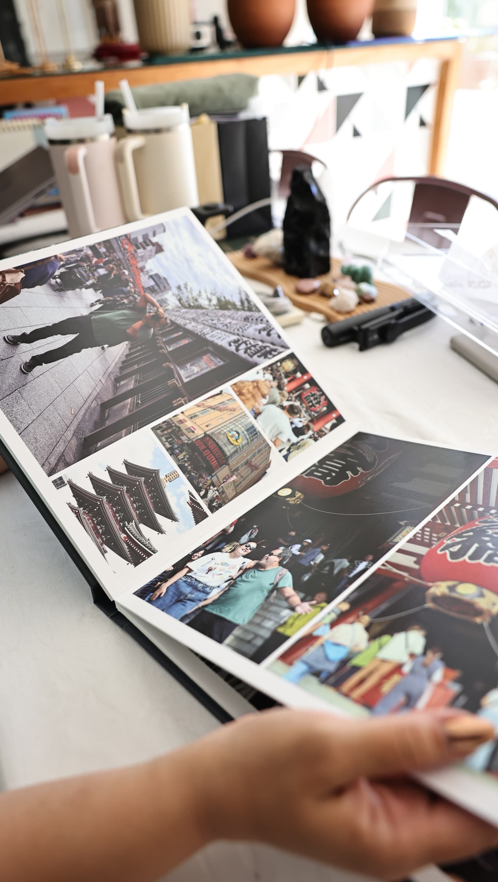 Álbum de viagem real aberto e sendo folheado, com fotografias impressas do Japão